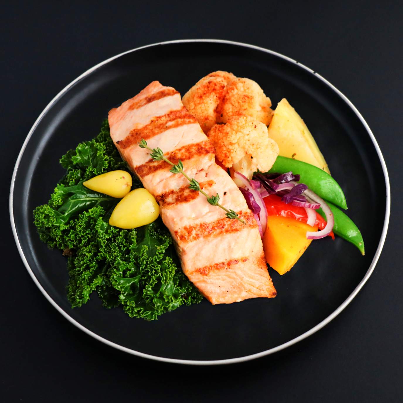 Grilled salmon slice with assorted vegetables on a black plate