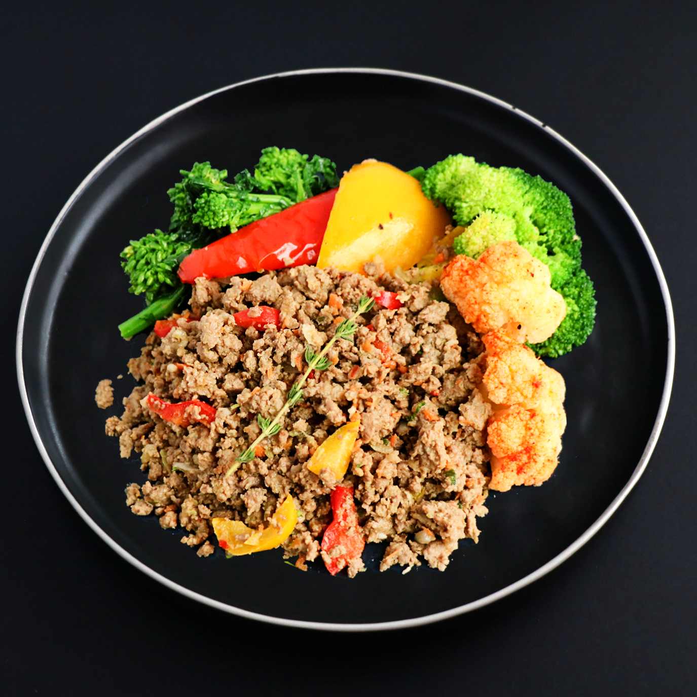 Ground lean beef with assorted vegetables decorated with herb on a black plate