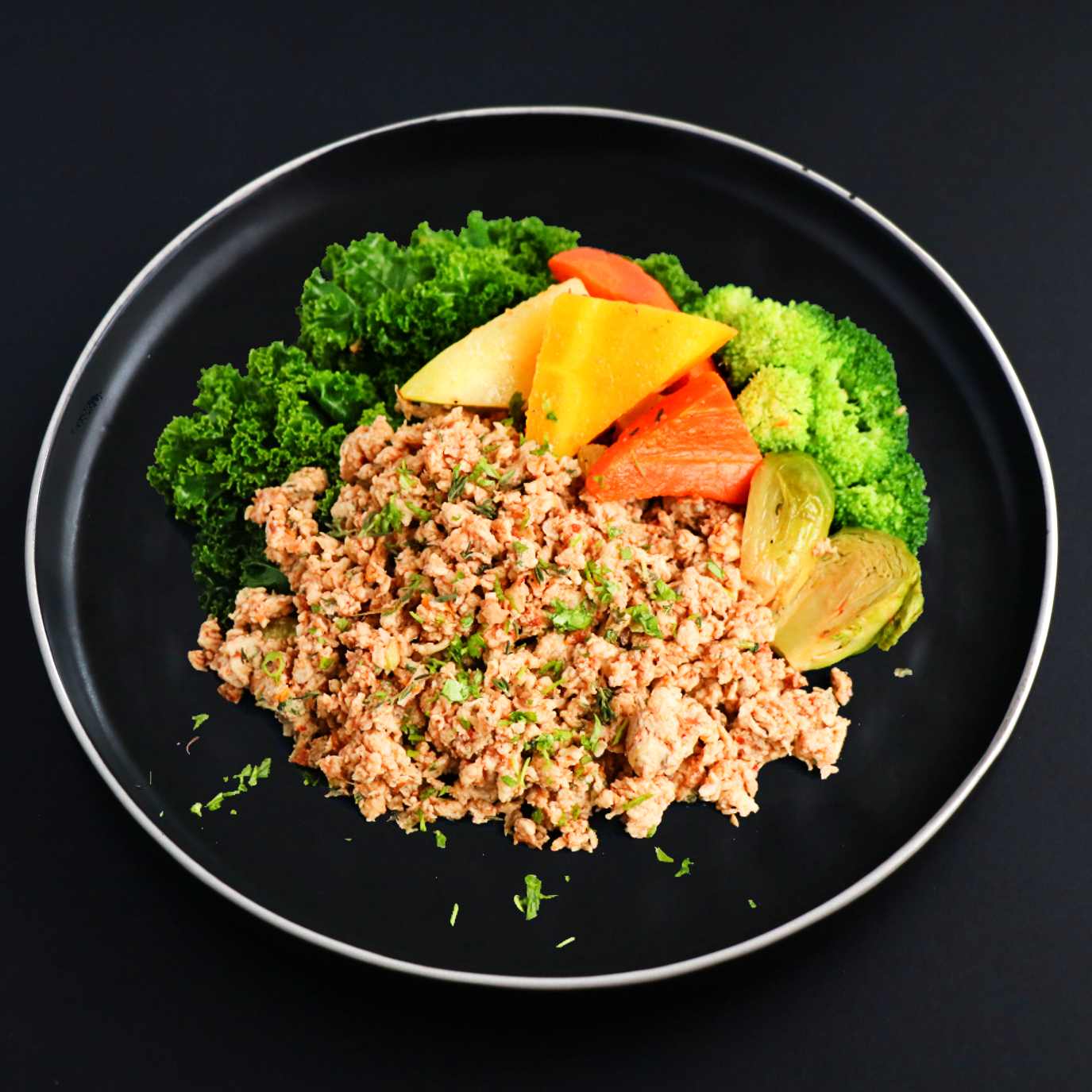 Lean ground turkey with a side of assorted vegetables sprinkled with parsley on a black plate