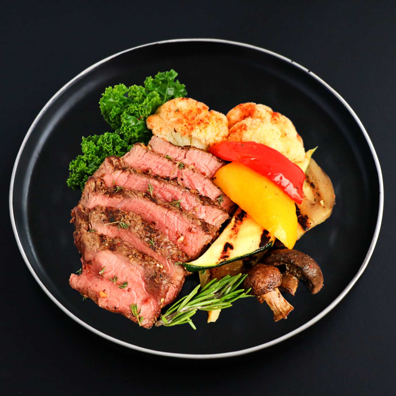 Grilled beef steak on a black plate with assorted veggies on the side