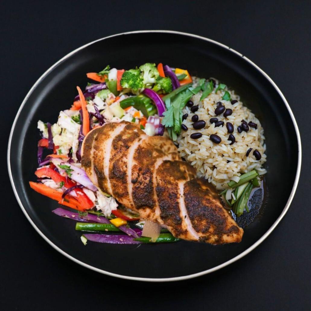 Juicy and tender piece of a sliced gourmet Jerk chicken breast accompanied by a side of black bean brown rice and assorted vegetables.
