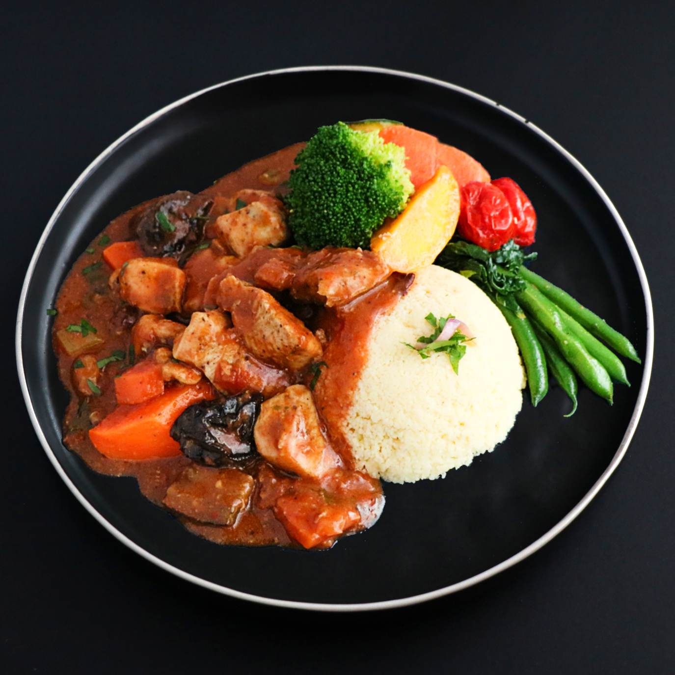 A plate of Gourmet Moroccan Turkey Stew with vegetables, couscous, and a side of green beans and broccoli.