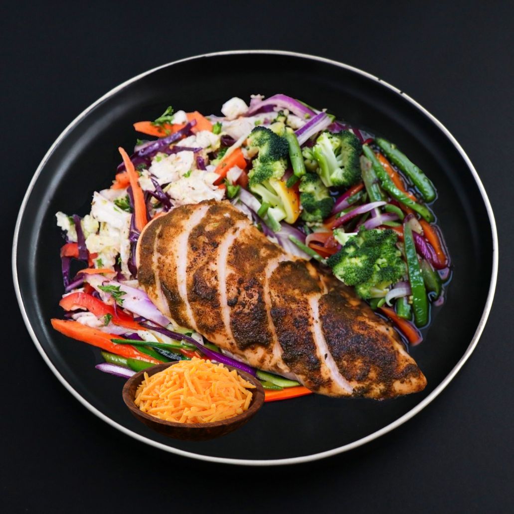Juicy and tender piece of Keto Jerk chicken breast that comes with a variety of vegetables and topped with Cheddar cheese on a black plate.