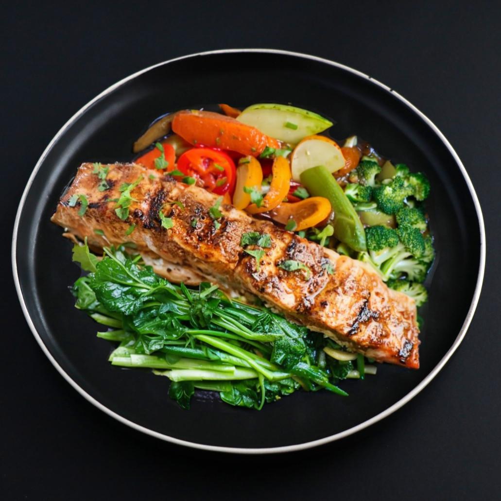 A piece of a juicy tandoori salmon garnished with parsley represents one of the balanced meal plan items and comes with assorted and leafy green vegetables.