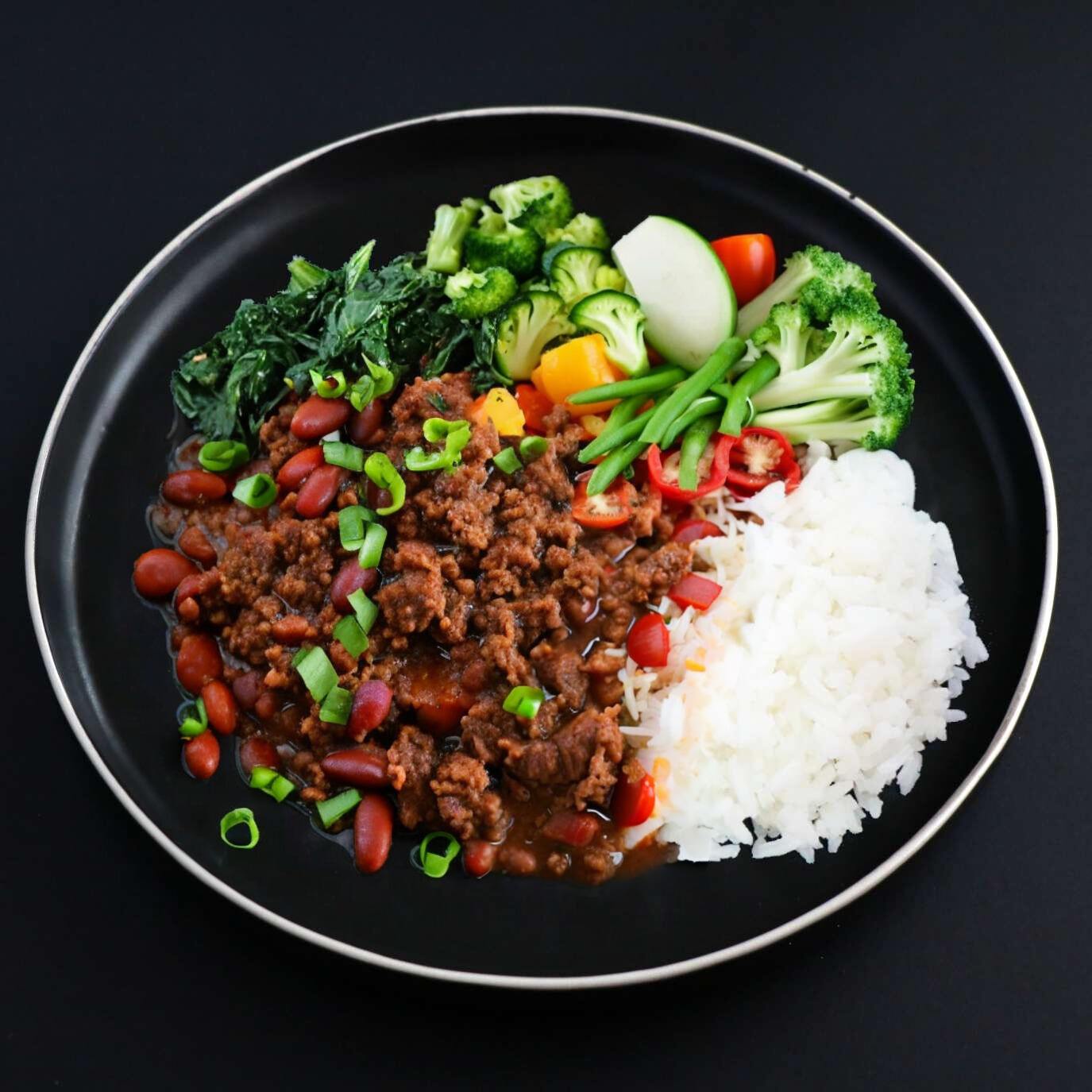 A plate of Gourmet beef chili with white rice topped with green onions, accompanied by a side of broccoli and vegetables.