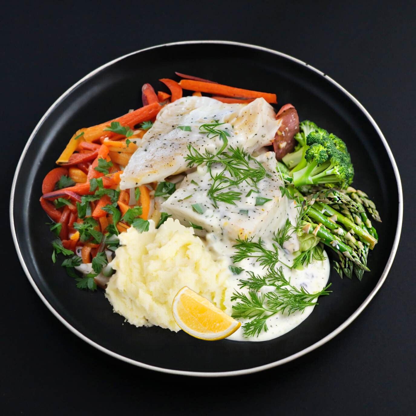 A plate of a Gourmet Lemon Dill Cod Fillet with mashed potatoes, accompanied by carrots, broccoli, and a slice of lemon.