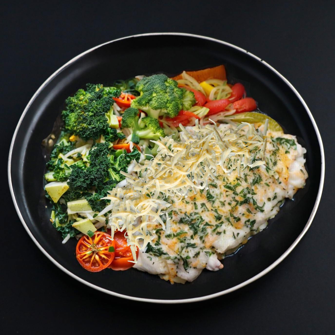 A plate of baked keto cod florentine with a side of steamed broccoli, carrots and green herbs on a black plate topped with shredded parmesan cheese.