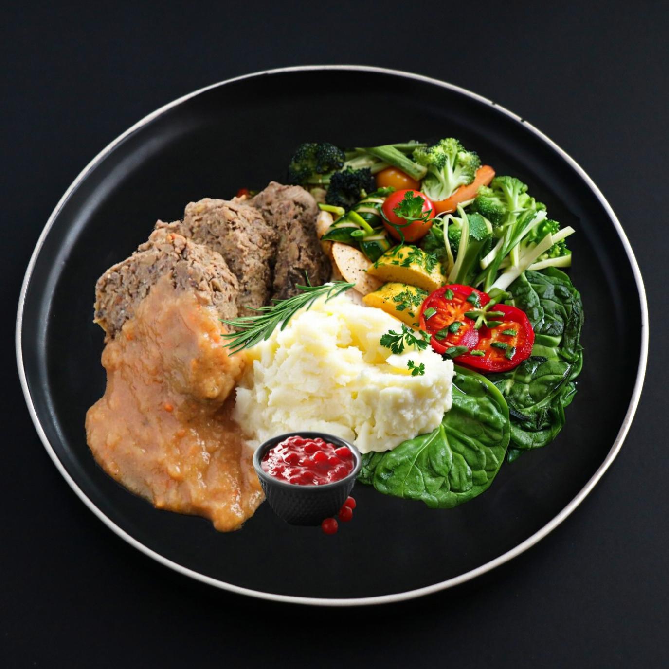 Lentil meatloaf is covered with homemade vegan gravy and sided with mashed potato and cranberry coulis, assortment of veggies complements this vegan meal presentation.
