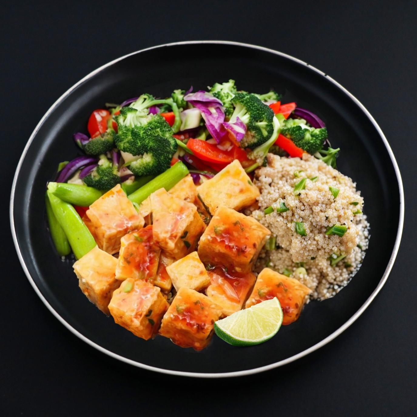 This vegan plate features cubes of organic tofu drenched in lime sweet chili sauce with a side of quinoa and assorted vegetables.