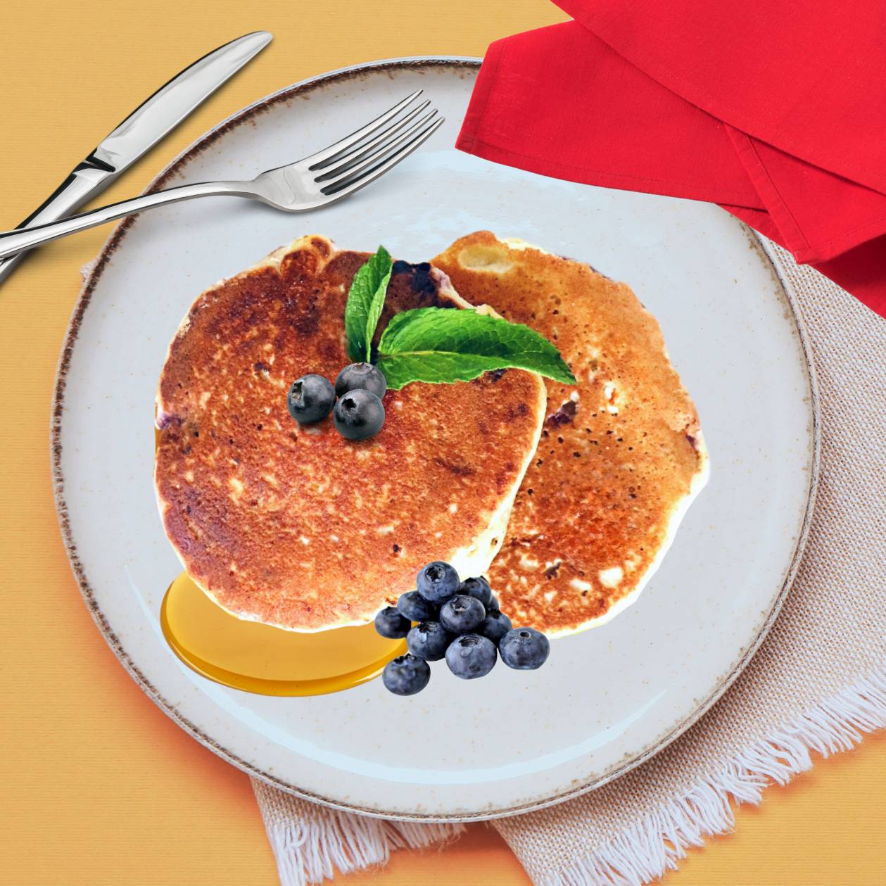 A plate with two vegan blueberry pancakes topped with syrup and a sprig of mint, alongside a cluster of blueberries on the side.