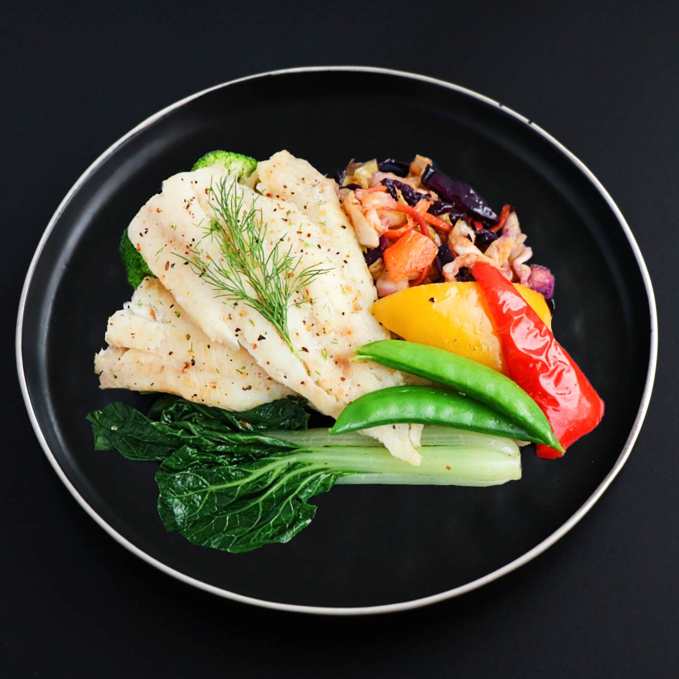 A baked cod fillet with roasted potatoes, bell peppers, and broccoli on a black plate, garnished with dill.