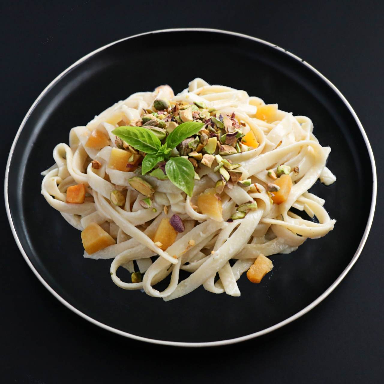 A plate of fettuccine pasta with creamy pistachio butternut squash sauce, garnished with pistachio nuts on a dark plate.