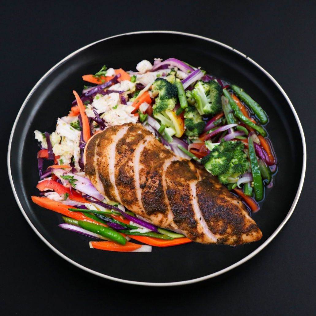Sliced jerk chicken breast from the balanced menu with assorted vegetables on a black plate