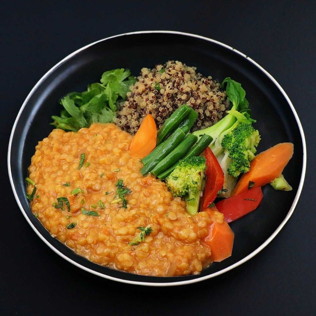 A plate of vegan red lentil curry served with brown rice topped with red lentils, accompanied by broccoli, carrot, and cilantro.