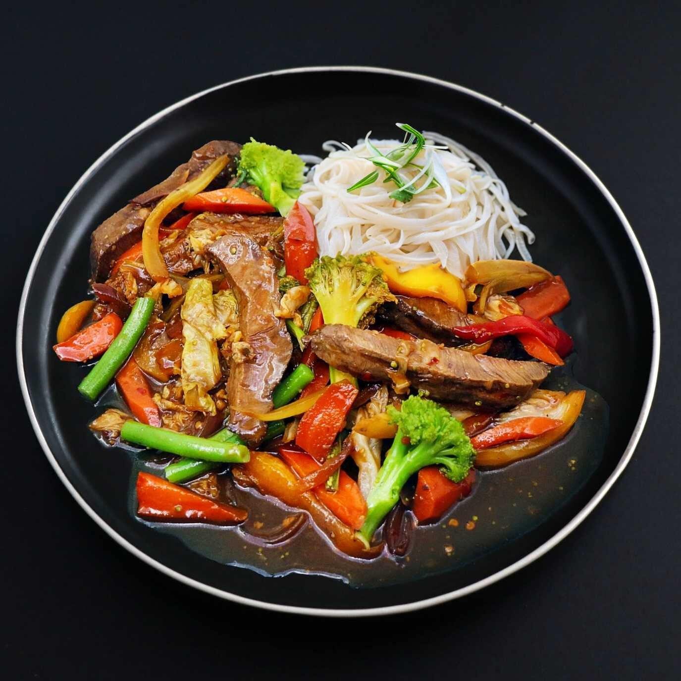 A plate of a Gourmet Beef Stir Fry with tender beef strips and crisp vegetables, served with rice noodles on the side.