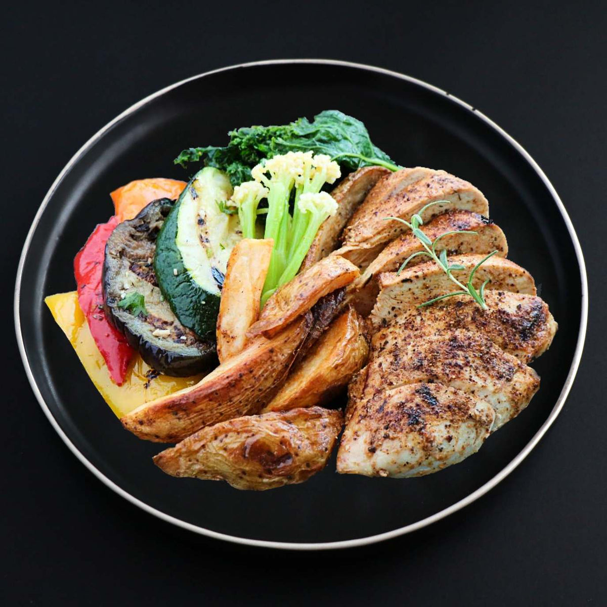 A gourmet plate containing Cajun chicken thighs served with roasted potatoes and assorted grilled vegetables.