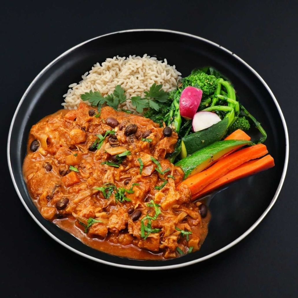 Plated dish with Mexican jackfruit curry, rice pilaf and vegetables on a black background.