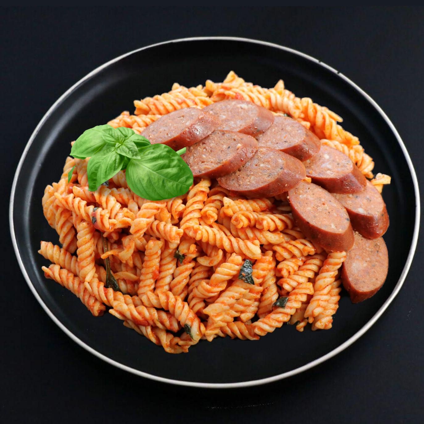 A plate of Fusilli Arrabiata with Beef Sausage, garnished with a basil leaf, on a dark background.