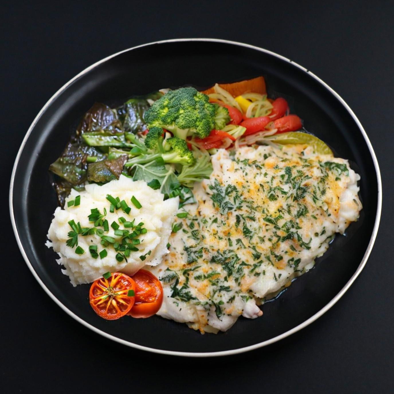 A plate of baked cod florentine with a side mashed potato and mixed vegetables, garnished with herbs and chives is presented on a black plate and is a part of the gourmet menu.