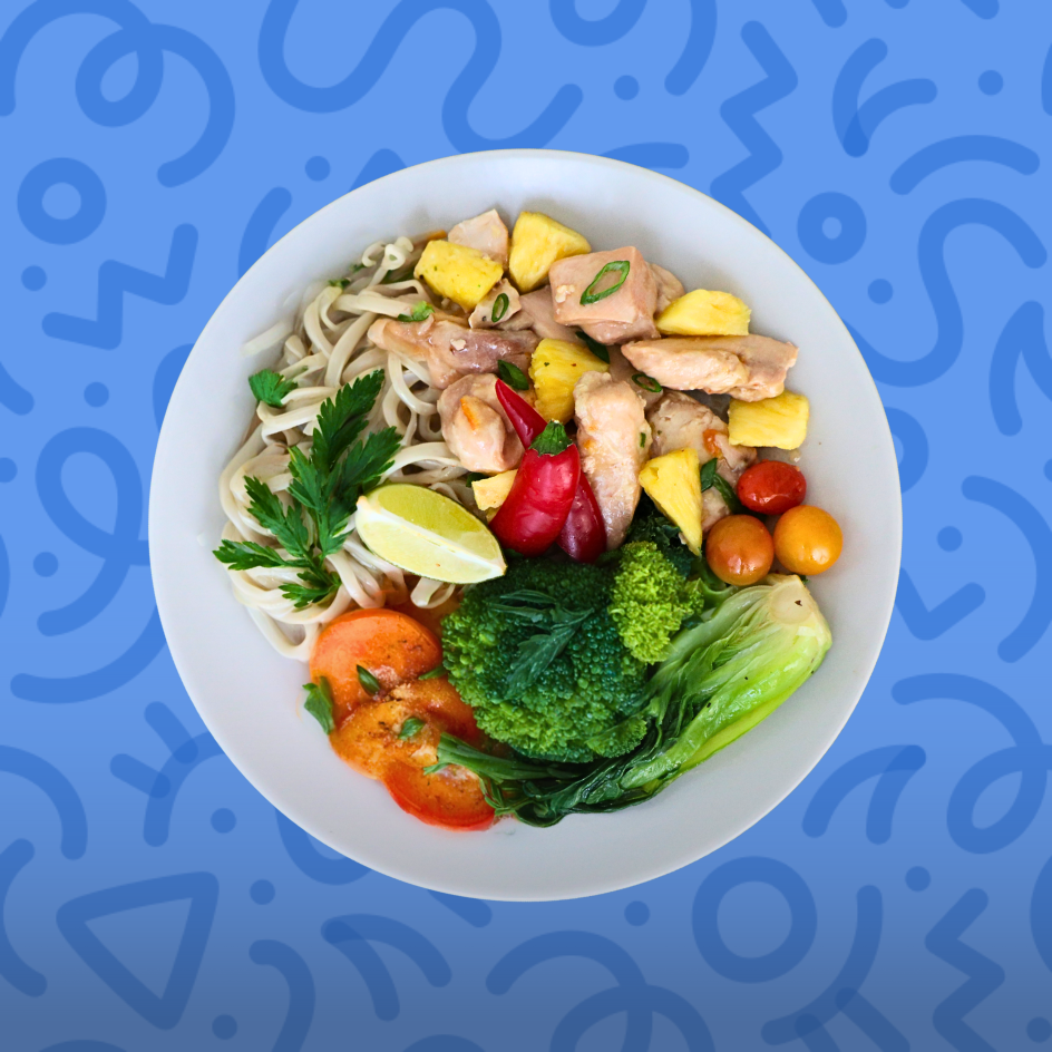 Healthy chicken noodle bowl with rice noodles, pineapple, broccoli, and bok choy on a blue background.