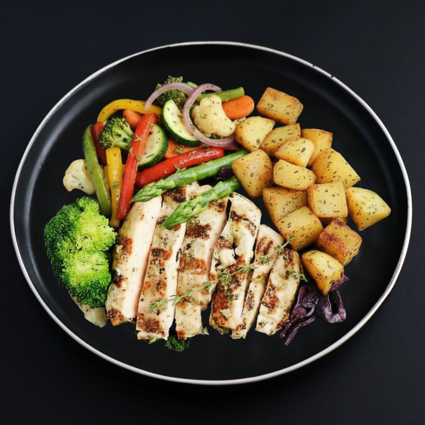 Plated dish with grilled chicken breast, roasted potatoes, and a variety of vegetables on a black background