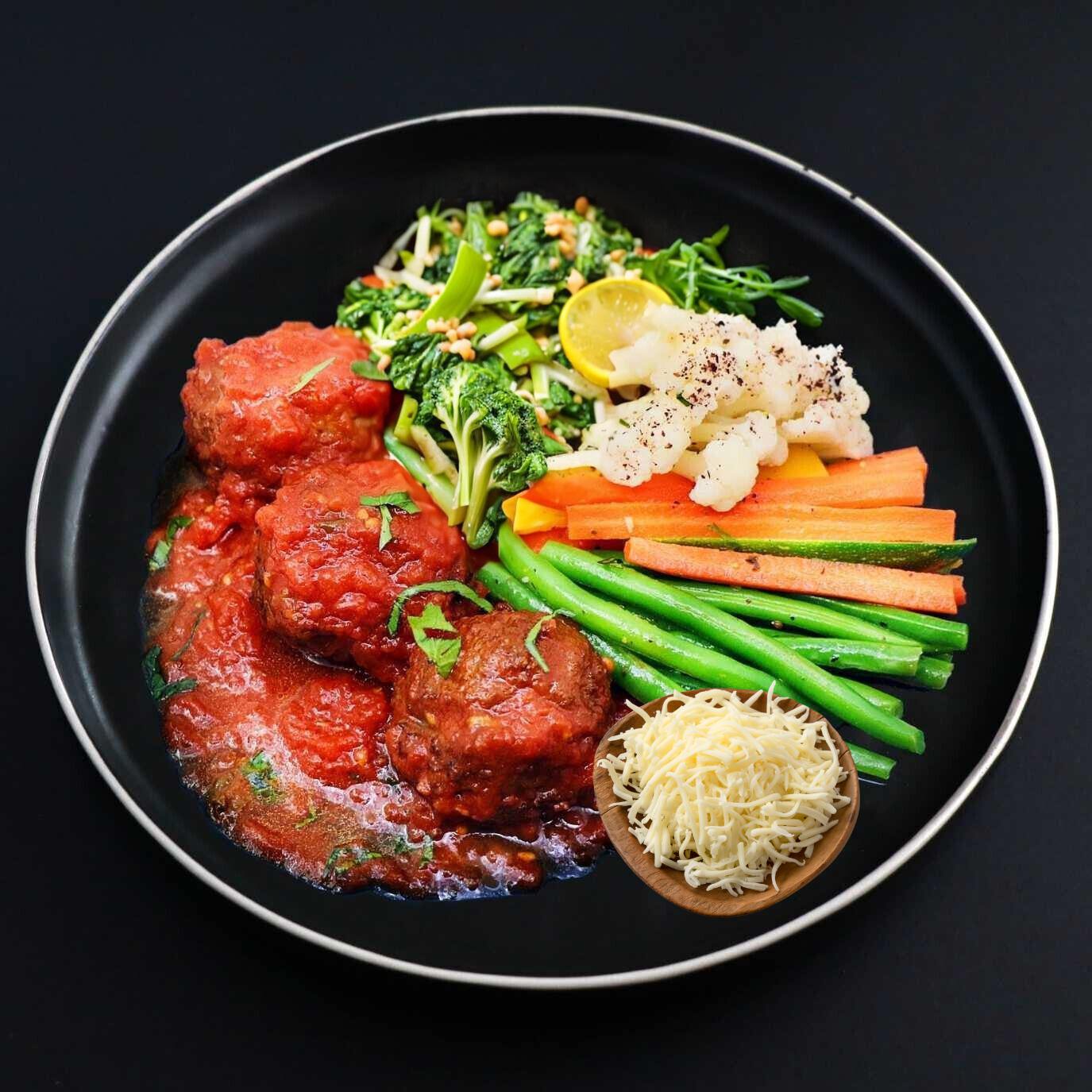 A plate of keto Italian meatballs topped with homemade authentic tomato sauce, mozzarella, served with a side of green beans, carrots, and other veggies.