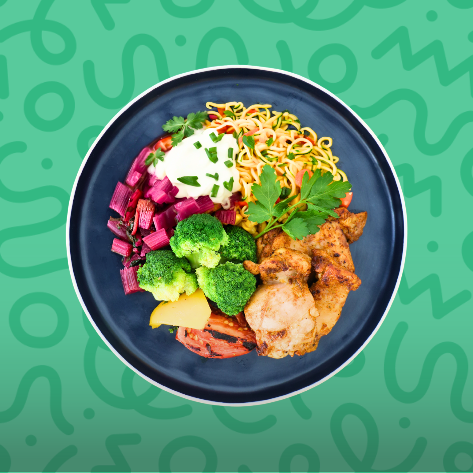 Keto grilled chicken bowl with sour cream, broccoli, sautéed purple cabbage, and zoodles on a green background.