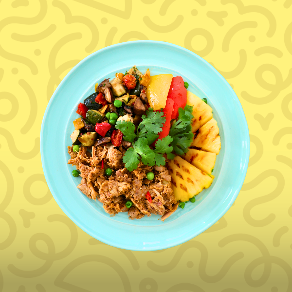 Paleo pulled chicken bowl with grilled pineapple, roasted zucchini, peppers, mushrooms, and fresh cilantro on a yellow background.