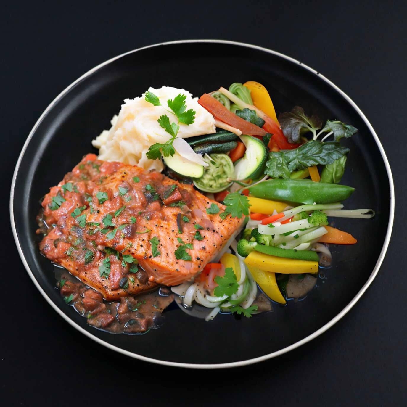 A plate of Gourmet Salmon Puttanesca with succulent salmon topped with a tangy tomato sauce, accompanied by mashed potatoes and a side salad.