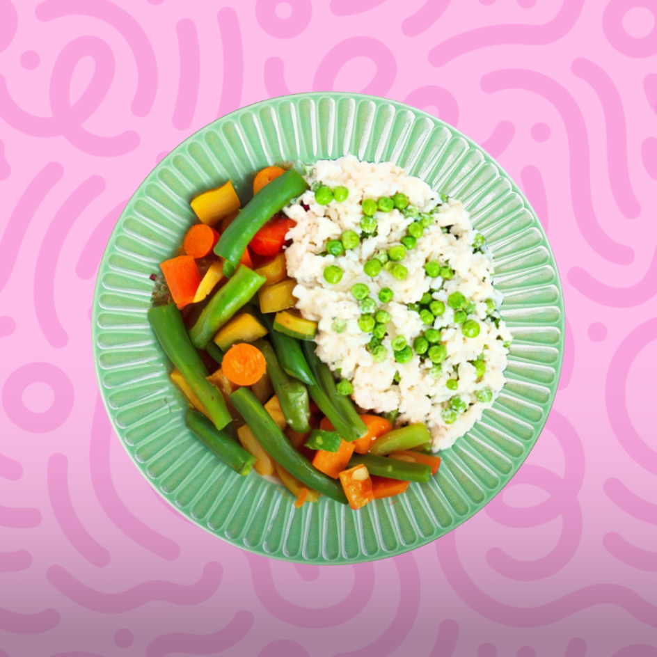 Vegan cauliflower rice bowl with green peas, steamed green beans, carrots, and squash on a pink patterned background.