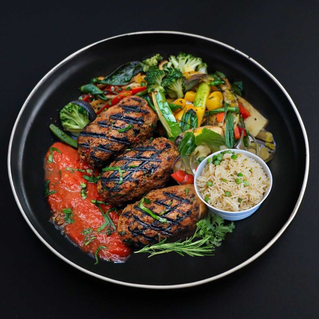 A plate containing gourmet grilled beef kafta kebabs with a side of rice pilaf and mixed vegetables.