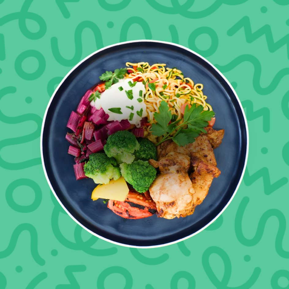 Keto grilled chicken bowl with sour cream, broccoli, sautéed purple cabbage, and zoodles on a green background.