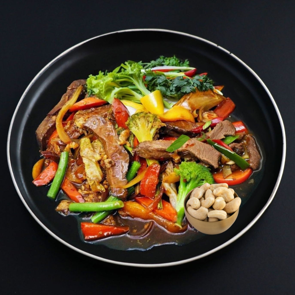 Keto Beef stir-fry dish with juicy and crispy vegetables on a black plate with a side roasted cashews.