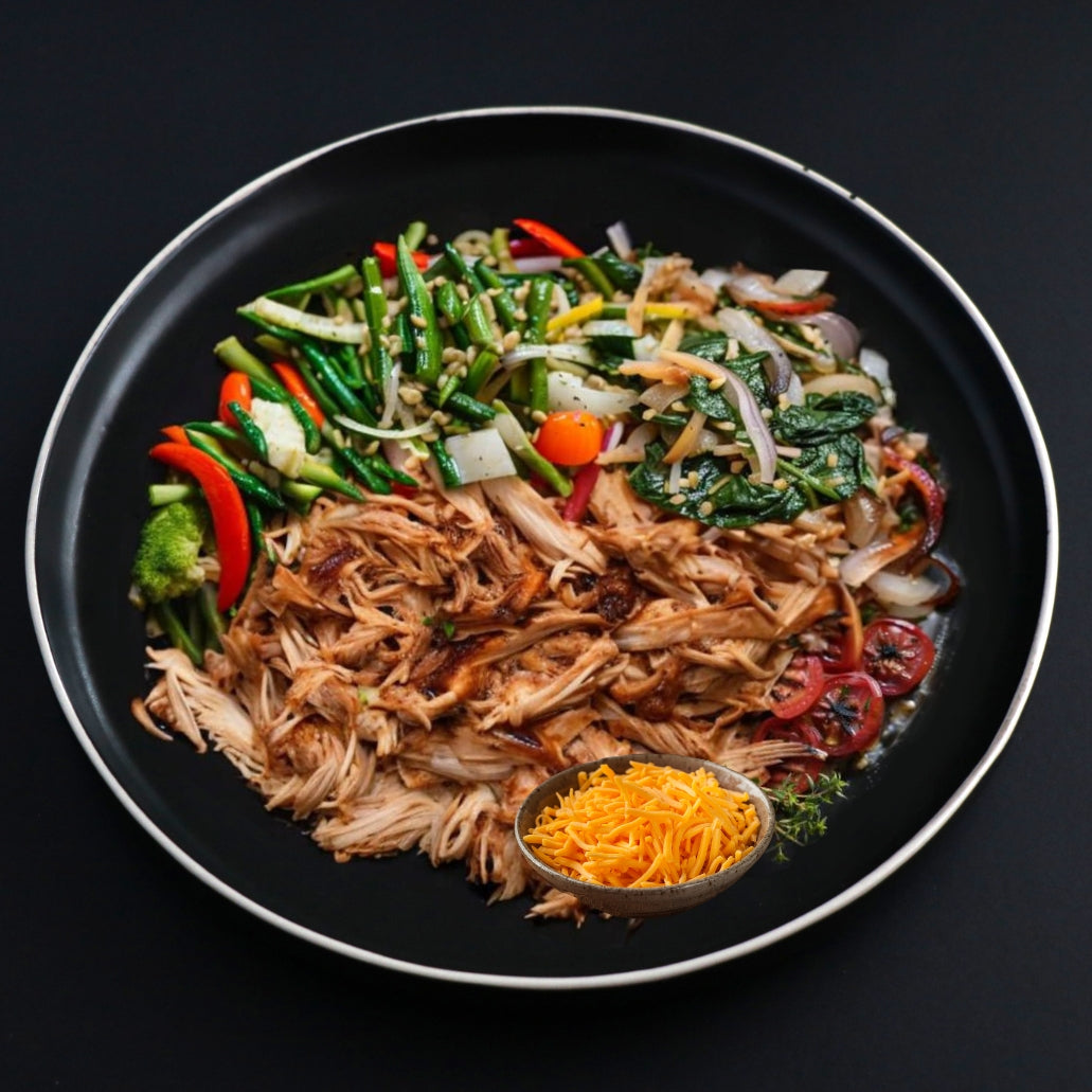 Keto barbeque pulled chicken dish that comes with a side of crispy and juicy veggies and topped with shredded cheddar cheese on a black plate.